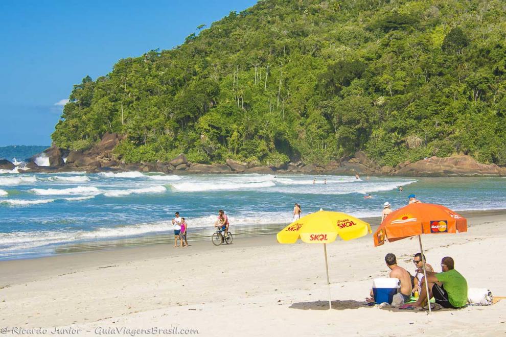 Imagem de uma família caminhando na beira da praia e uma pessoa andando de bicicleta.